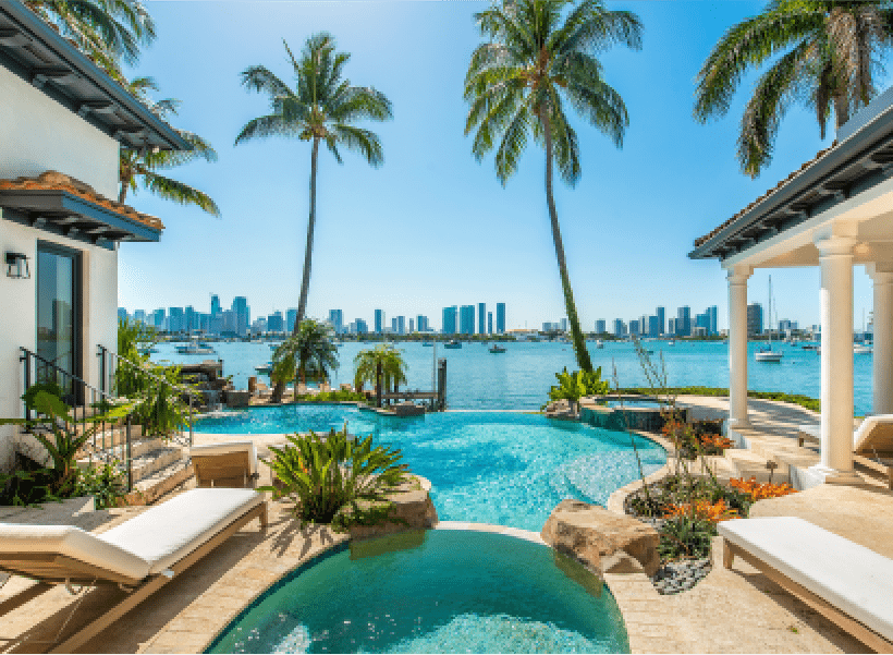 A pool area with lounge chairs, palm trees, and a city skyline in the background.